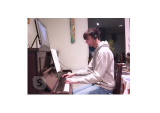 Image of pupil Tristan playing piano and using laptop with earphones in online piano lesson